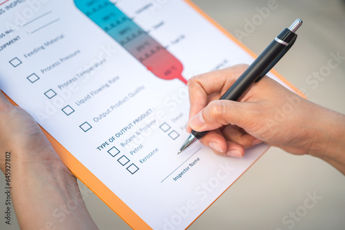 Action of a chemical engineer is using the pen to checking on oil refinery distillation process inspection form. Industrial working scene,close-up and selective focus.