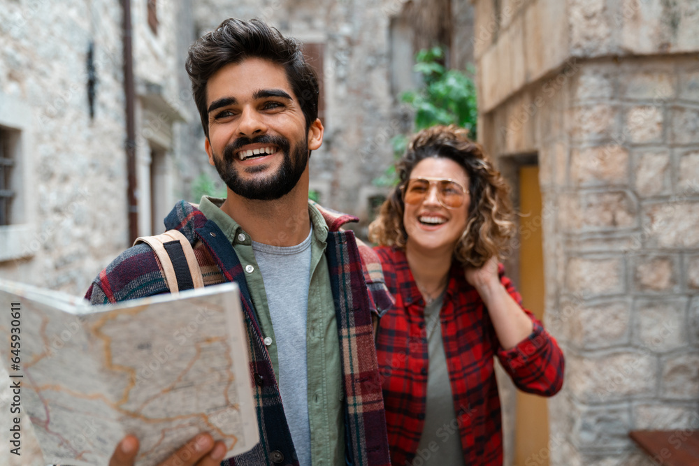 Beautiful young couple walking with a map in the city. Two friends spending vacation by exploring the streets of Mediterranean old town. Smiling man holding map and guiding his girlfriend. Beautiful young couple walking with a map in the city. Two friends spending vacation by exploring the streets of Mediterranean old town. Smiling man holding map and guiding his girlfriend.