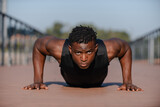 Concentrated young African athlete in sportswear doing push-ups while exercising outdoors