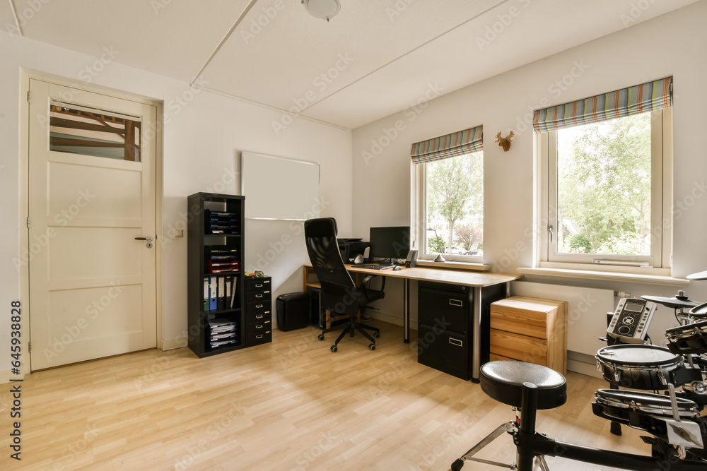 Fototapeta premium a home office area with wood floors and white walls, including a desk, chair, filing cabinet, computer monitor and other items