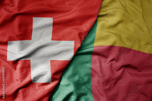 big waving national colorful flag of switzerland and national flag of benin .