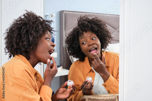 Happy african woman applying vaseline in front of the mirror.