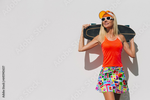 Portrait of female with her skateboard in sportware against white wall for copy space © Oleg