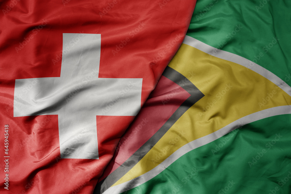 big waving national colorful flag of switzerland and national flag of guyana .