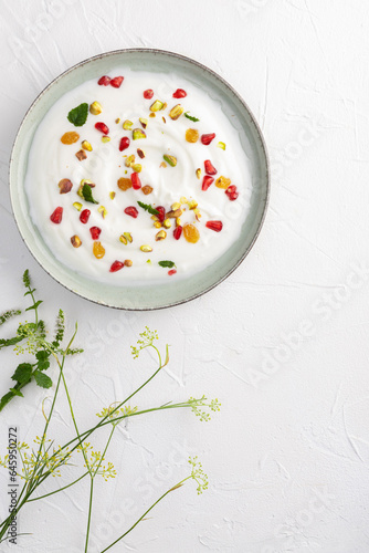 Yogurt with raisins, pistachios and pomegranate seeds in plate on green background. top view. Healthy breakfast, healthy eating concept