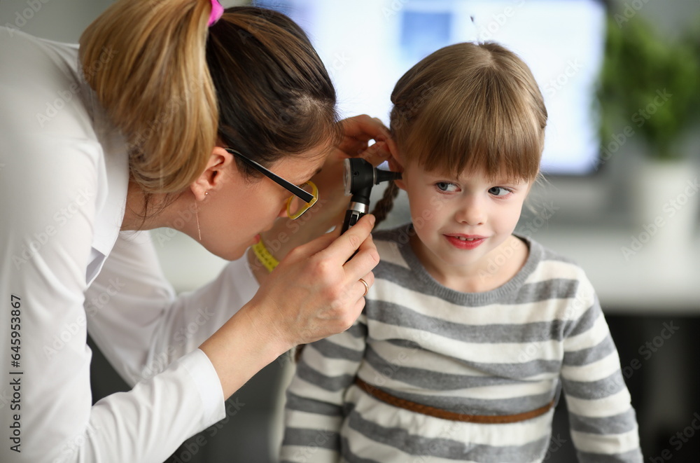 Portrait of joyful girl sitting in clinic office and looking away with happiness. Professional therapist watching in child ear with special utility. Health checkup concept Portrait of joyful girl sitting in clinic office and looking away with happiness. Professional therapist watching in child ear with special utility. Health checkup concept
