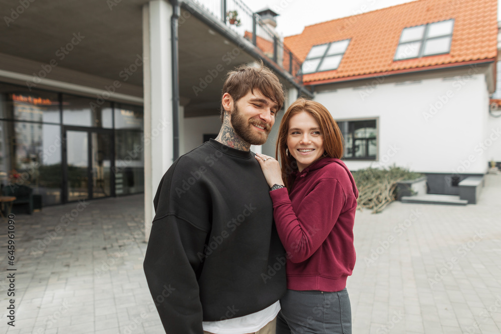 Beautiful fashionable happy couple hipster handsome man with beard and tattoo and pretty redhead woman in stylish pullover walks on the street Beautiful fashionable happy couple hipster handsome man with beard and tattoo and pretty redhead woman in stylish pullover walks on the street