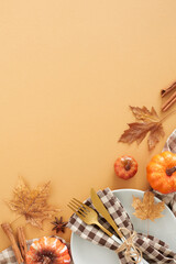 Stunning autumn-themed table decor. Top view vertical shot of plate, cutlery, tablecloth, pumpkins, cinnamon sticks, anise, acorns, fallen leaves on pastel brown background with ad space