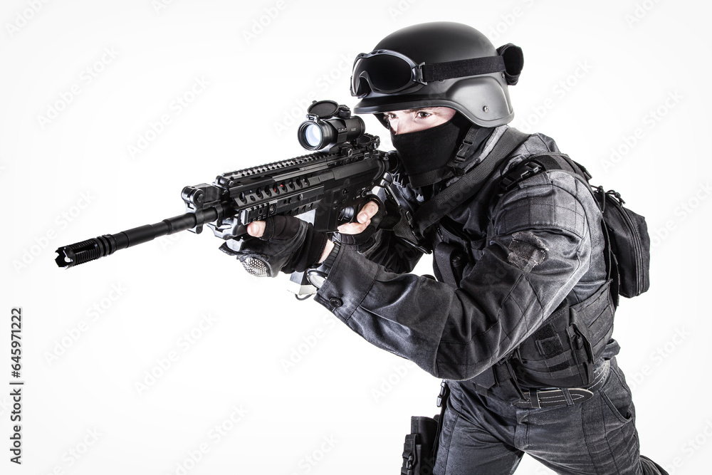 Spec ops police officer SWAT in black uniform aiming service rifle, studio shot