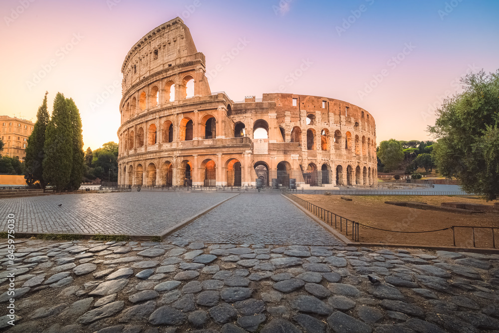 Iconic Flavian Amphitheatre, the ancient Roman Colosseum, a famous tourist landmark illuminated at twilight and dawn in historic Rome, Italy.