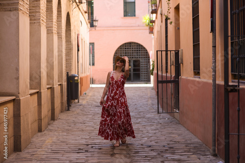 Young and beautiful blonde woman with sunglasses and straw hat on her head walking in the historical centre of seville. The woman is on holiday and enjoys the city. The woman is happy. © @skuder_photographer