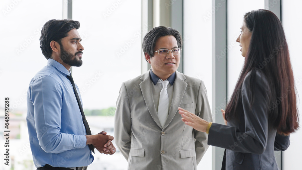 Three colleagues talking and discussing about work at office. Group of businesspeople talking to each other while standing at modern office. Business meeting Three colleagues talking and discussing about work at office. Group of businesspeople talking to each other while standing at modern office. Business meeting