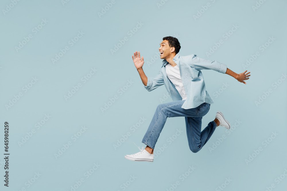 Full body side view young man of African American ethnicity he wears shirt casual clothes jump high run fast hurry up, be in rush isolated on plain pastel light blue cyan background studio portrait.