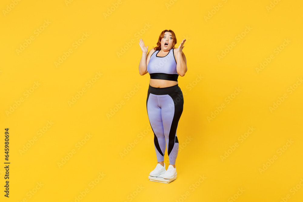 Full body shocked young plus size big fat fit woman wears blue top warm up train stand on scales check result spread hands isolated on plain yellow background studio home gym. Workout sport concept. Full body shocked young plus size big fat fit woman wears blue top warm up train stand on scales check result spread hands isolated on plain yellow background studio home gym. Workout sport concept.