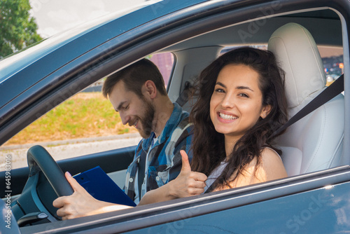 Smiling lady showing thumbs up sign while studying to drive while male instructor filling out the form. Driving test, driver courses, exam concept © Nataliya