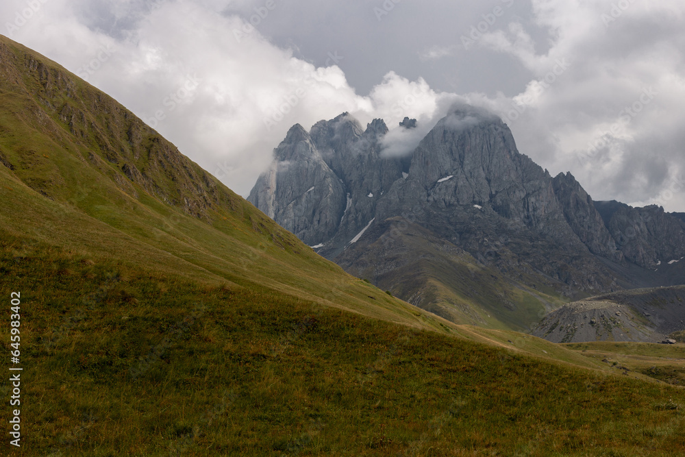 Picturesque view of the rocky cloudy Chaukhi Mountain and green hills in Georgia