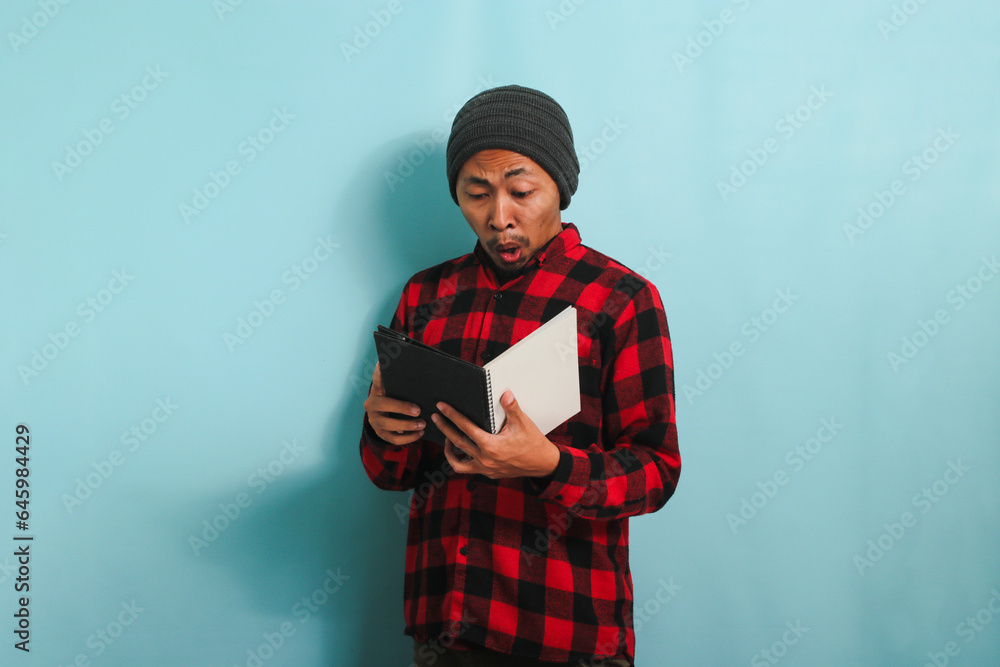 Confused young Asian male student looks shocked, not prepared for exams, isolated on blue background Confused young Asian male student looks shocked, not prepared for exams, isolated on blue background