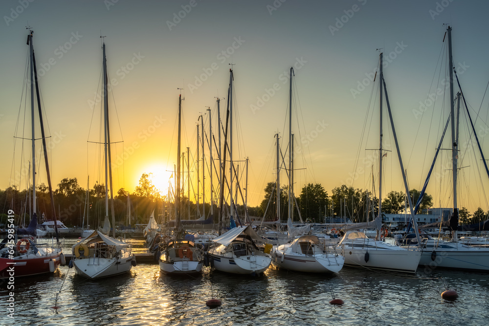 Beautiful sunset with sunrays illuminating luxury yachts and boats moored in a row at Szczecin Dabie marina, Poland