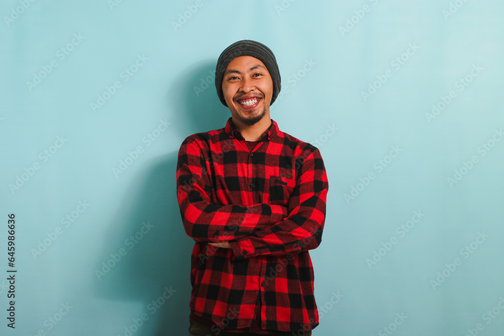 Fototapeta premium Confident young Asian man is looking at the camera with his arms crossed isolated on blue background