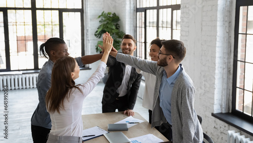 Foto Excited multiracial colleagues give high five celebrate shared company group win