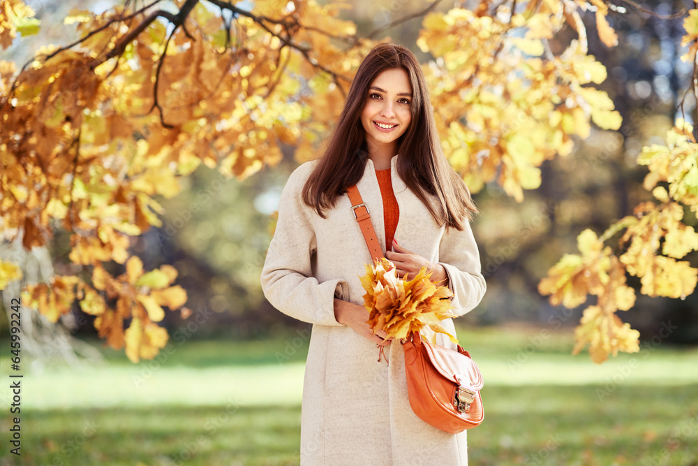Autumn portrait of a beautiful happy smiling woman with yellow maple leaves in a white coat in the park Autumn portrait of a beautiful happy smiling woman with yellow maple leaves in a white coat in the park