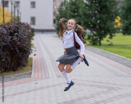 Happy caucasian girl in uniform and with a backpack jumping outdoors after school.