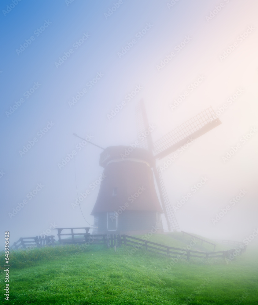 Landscape with windmill during fog. Holland. Dawn during a thick fog. Agricultural fields and pastures. Summer landscape in the Netherlands.