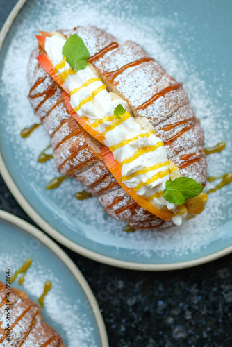 Sweet croissant sandwich dessert filled with whipped cream mixed with custard on blue plate 