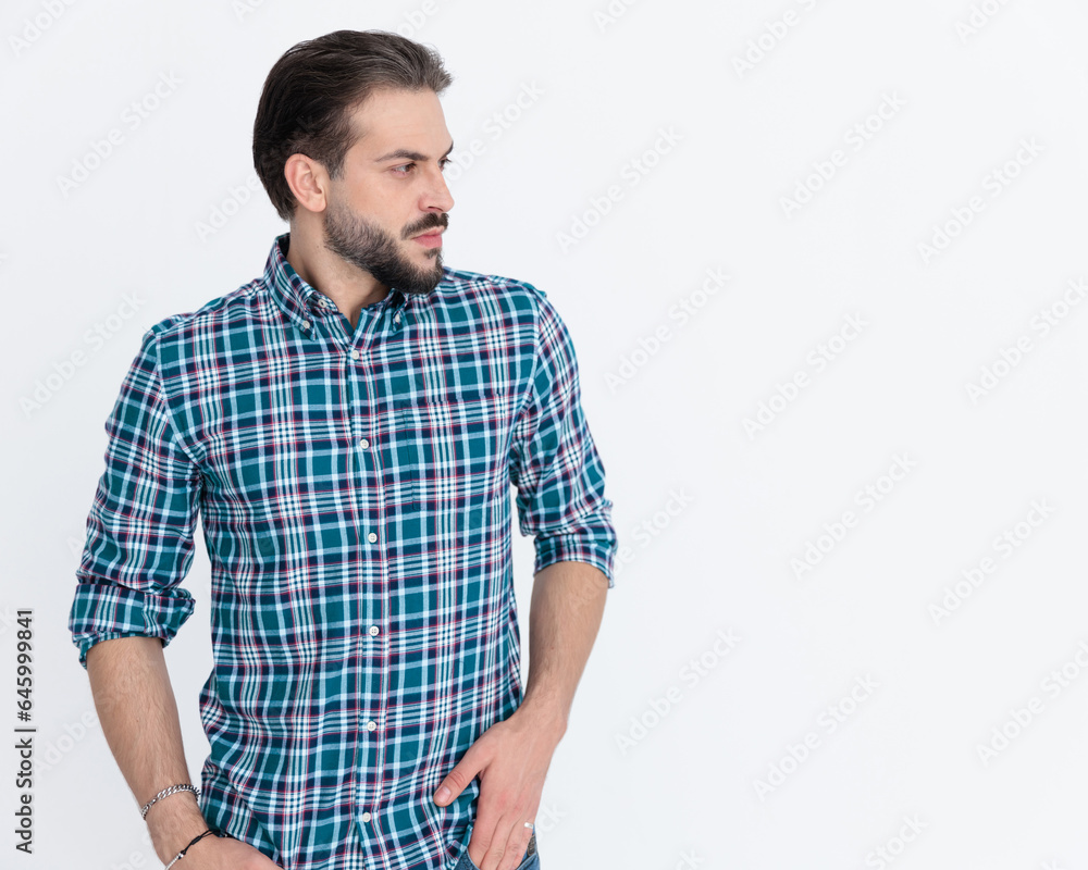 young casual man in plaid shirt holding hands in pockets and looking to side young casual man in plaid shirt holding hands in pockets and looking to side
