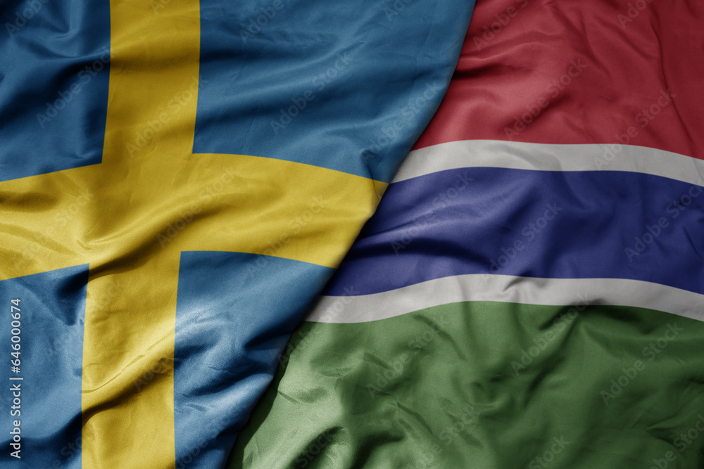 big waving national colorful flag of sweden and national flag of gambia .