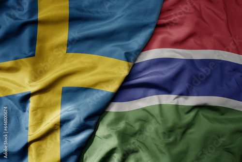 big waving national colorful flag of sweden and national flag of gambia .