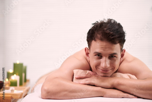 Portrait of smiling young man relaxing on bed after back massage