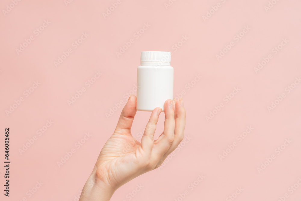 White bottle (plastic tube) in hand on pink background. Packaging for vitamins, pill or capsule, or supplement. Mockup for product branding White bottle (plastic tube) in hand on pink background. Packaging for vitamins, pill or capsule, or supplement. Mockup for product branding