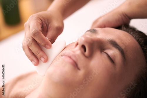 Cosmetologist using gua sha when massaging face of man