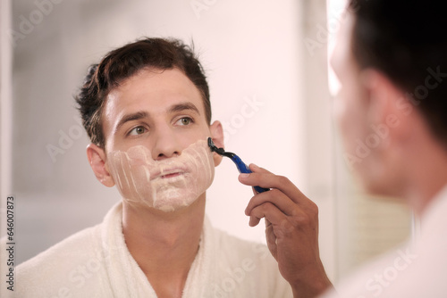 Portrait of young man shaving face after morning shower