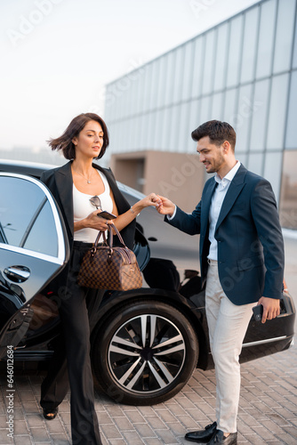 Businessman helps gently a woman to get out of a car, arrived by luxury vehicle for some event at evening. Concept of transportation and business lifestyle