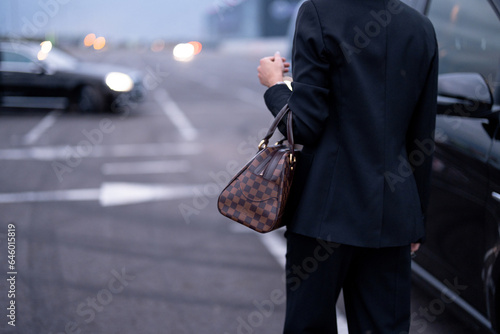Businesswoman carries luxury handbag, walking to car on parking lot. Close-up on bag