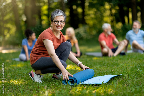 Smiling Senior Woman Rolling Yoga Mat After Group Lesson Outdoors