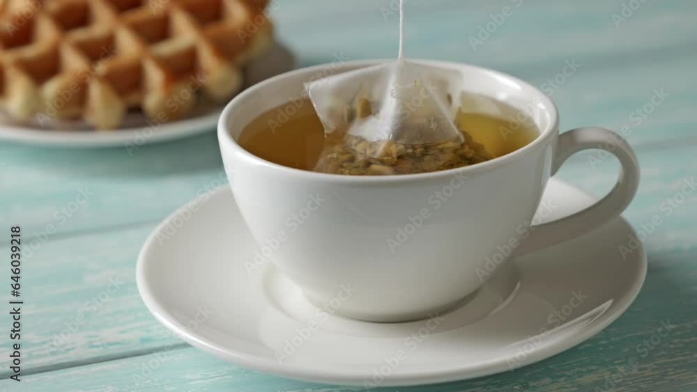 Preparation of bagged chamomile herbal tea in a cup. Tea and waffle dessert. Preparation of bagged chamomile herbal tea in a cup. Tea and waffle dessert.