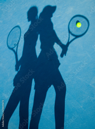 hadows of two girls with rackets on a blue court	 photo