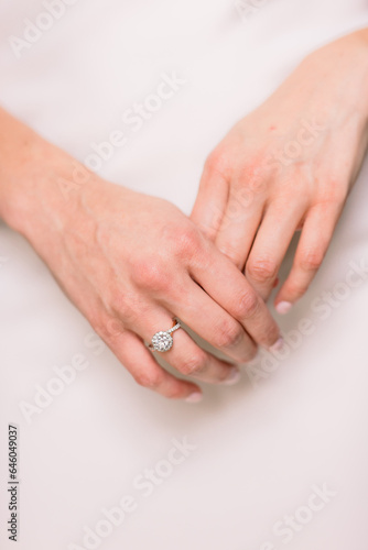 A worried bride on her wedding day holds her hands together, showing off her engagement ring, against the backdrop of her white wedding dress