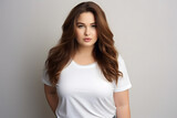 Young beautiful plus size woman model with long hair in white t-shirt posing on light grey background.