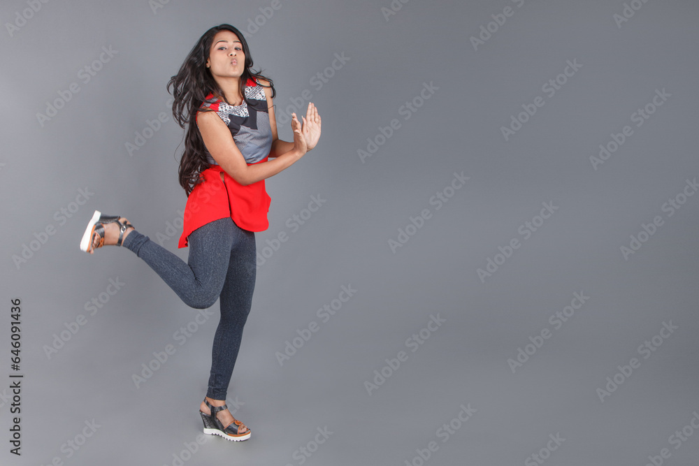Studio shot of a young, beautiful Indian female model in casual wear wearing red and grey designer top and blue jeans against grey background. Female model. Fashion Portrait.