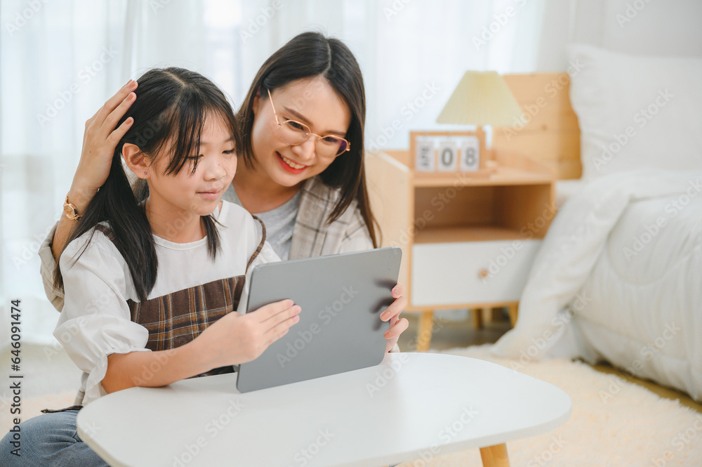 Asian schoolgirl with mother using tablet to study online at home Happy student with education looking at tablet front Watch the webinar online course homework Asian schoolgirl with mother using tablet to study online at home Happy student with education looking at tablet front Watch the webinar online course homework