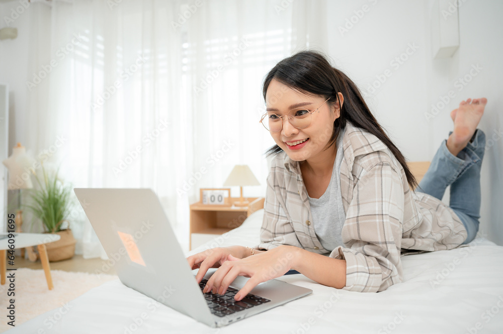 A woman freelance translator who is happy to work She lies on her bed playing on her laptop while chatting online remotely on her bedside laptop at her house. A woman freelance translator who is happy to work She lies on her bed playing on her laptop while chatting online remotely on her bedside laptop at her house.
