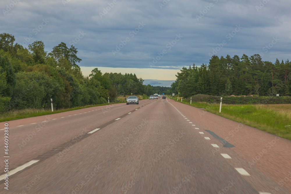 Asphalt road with green trees on both sides merging with blue cloudy sky. Sweden. Asphalt road with green trees on both sides merging with blue cloudy sky. Sweden.