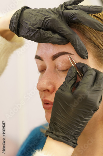 Portrait of a woman having her eyebrows plucked with tweezers in a beauty salon. © Dzmitry