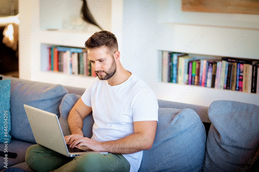 Handsome man wearing casual clothes and using laptop at home Handsome man wearing casual clothes and using laptop at home