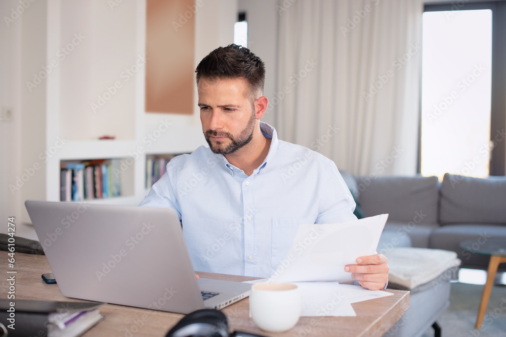 Mid aged man sitting at tabla and using laptop for work at home Mid aged man sitting at tabla and using laptop for work at home