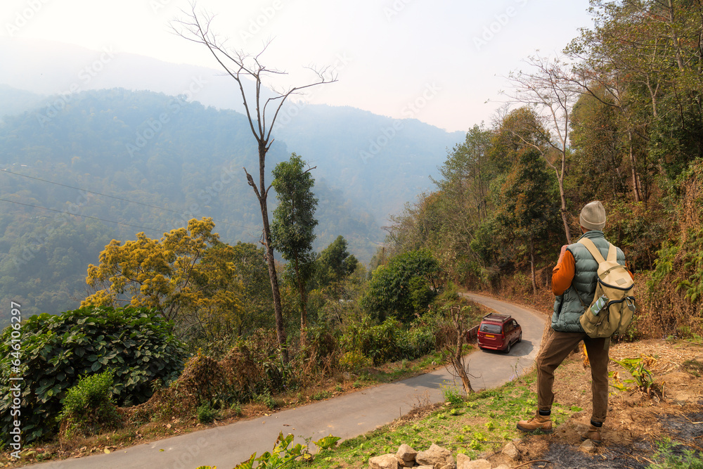 Fototapeta premium Male tourist enjoys an aerial view of a mountain road amidst scenic Himalaya mountain landscape near Tinchuley, a scenic hill station at Darjeeling, India